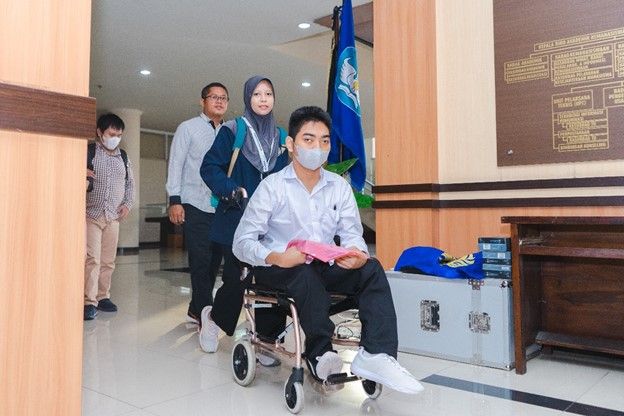 Didampingi dosen dan mahasiswa, peserta disabilitas, Akbar Pratama tampak semangat memasuki ruangan tes UTBK di Training Center, Rektorat UNESA.