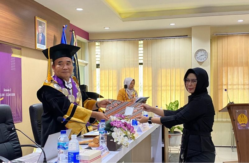 Dekan FIP sebagai ketua dewan penguji menyerahkan berkas kelulusan doktor bidang teknologi pendidikan kepada promovenda.